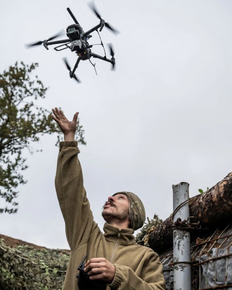 Ukrainian soldier in olive fleece reaching up to launch a drone against an overcast sky